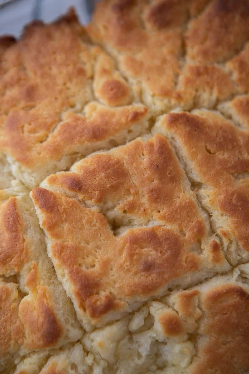 Close-up overhead view of butter swim biscuits in their baking dish showing the golden brown, slightly craggy, bubbly tops and crispy edges where the score lines separated during baking.