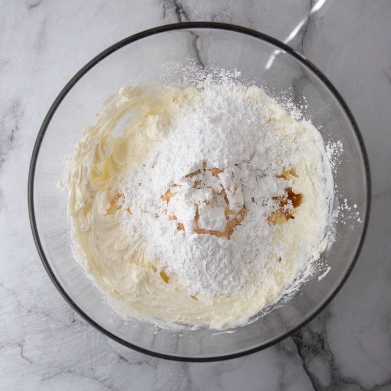 Ricotta mixture beaten until fluffy in a glass bowl. The creamy, cloud-like texture comes from whipping the cheeses with powdered sugar and vanilla.