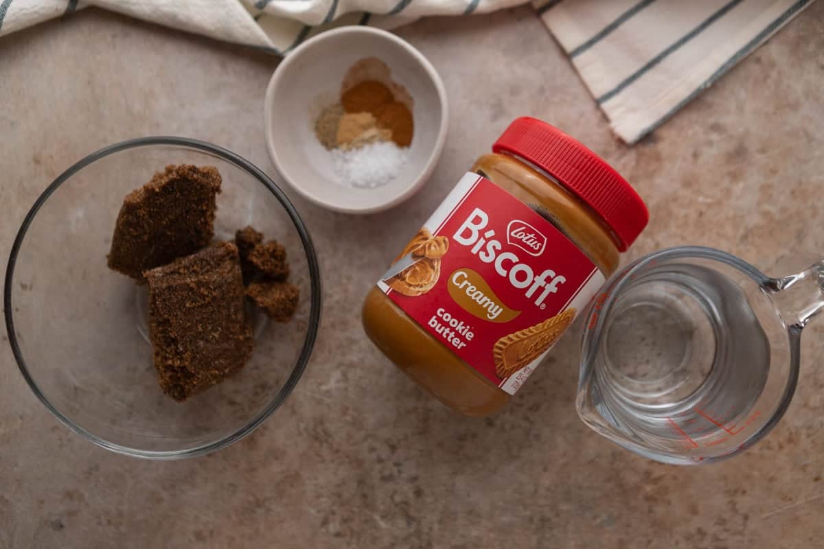 Ingredients for cookie butter coffee syrup including Lotus Biscoff spread, dark brown sugar, spices, and water measured out in bowls.