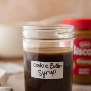 Homemade cookie butter coffee syrup in a labeled mason jar with a jar of Lotus Biscoff cookie butter in the background.