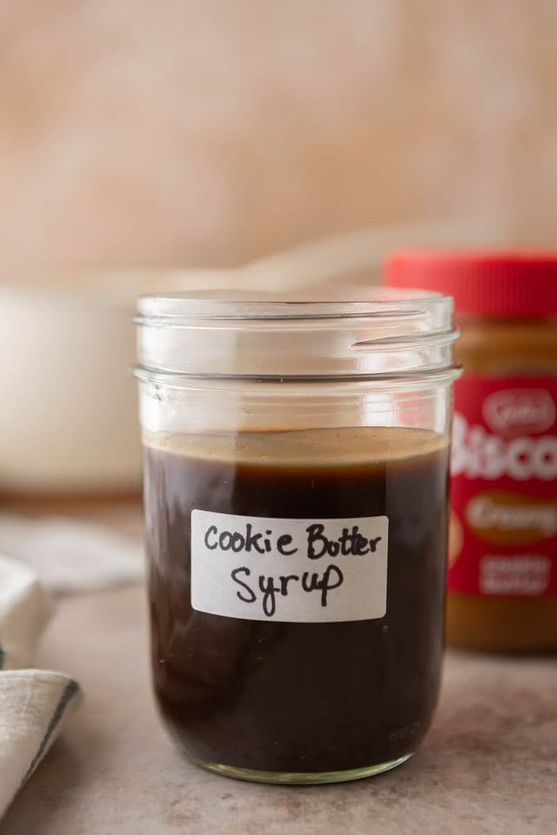 Homemade cookie butter coffee syrup in a labeled mason jar with a jar of Lotus Biscoff cookie butter in the background.