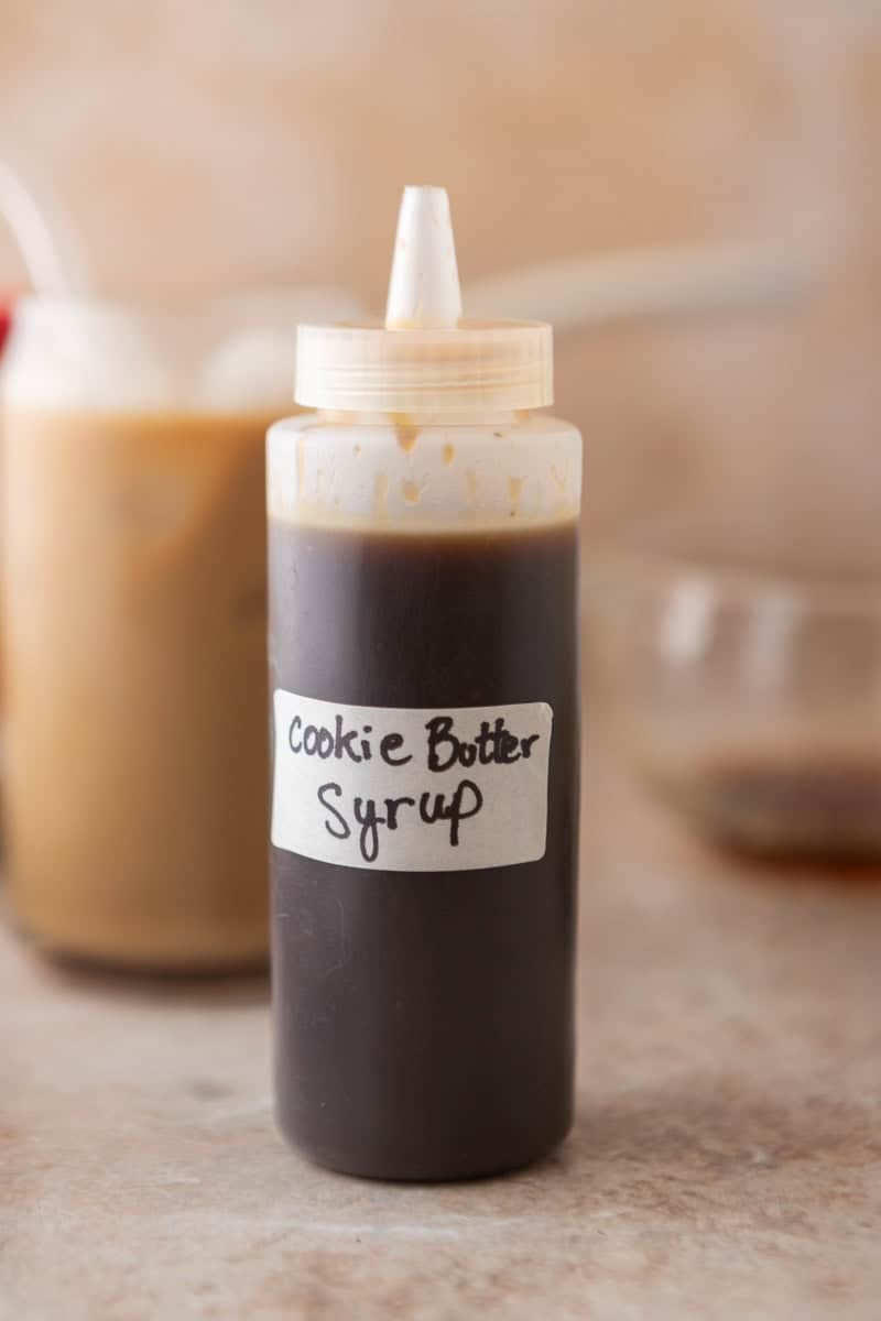 Homemade cookie butter coffee syrup in a squeeze bottle with a cookie butter iced latte in the background.