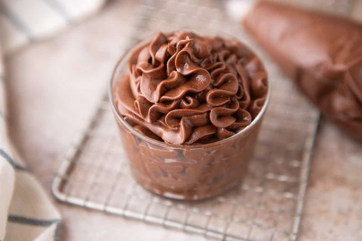 Chocolate cream cheese frosting piped into a small glass jar on a wire cooling rack