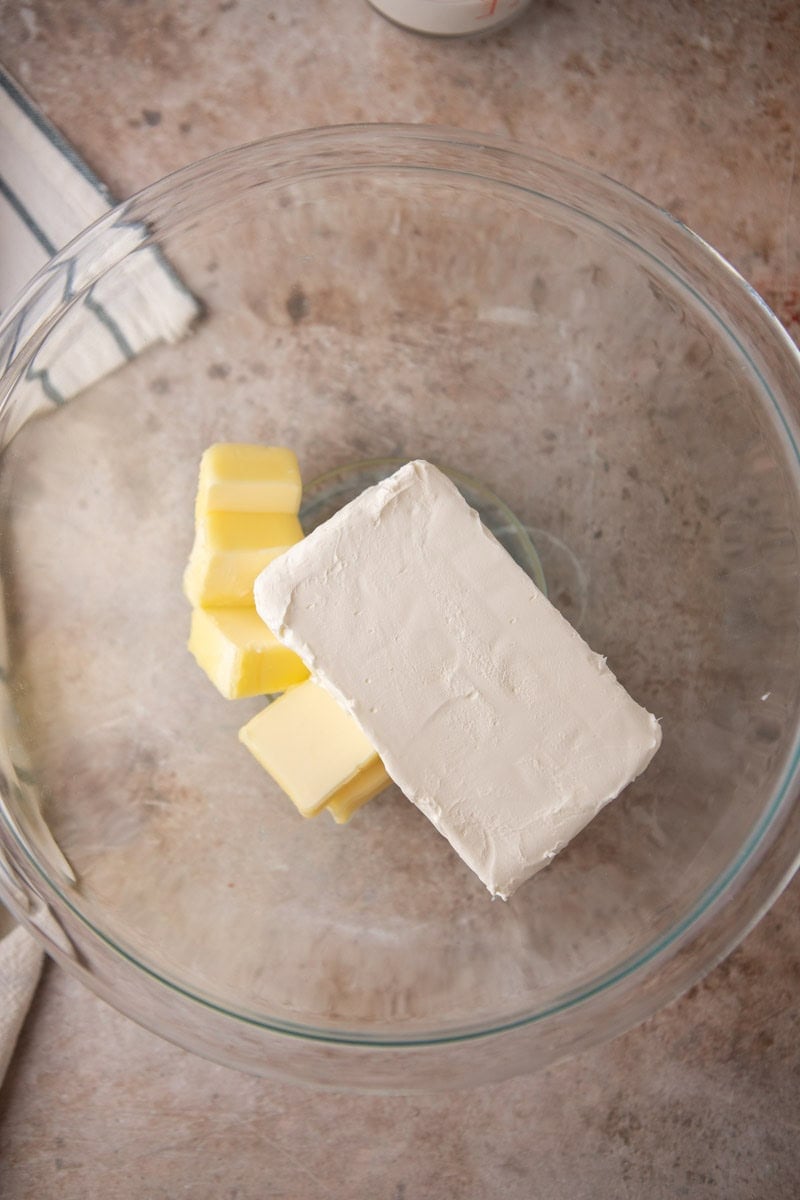 Block of cream cheese and cubes of softened butter in a glass mixing bowl