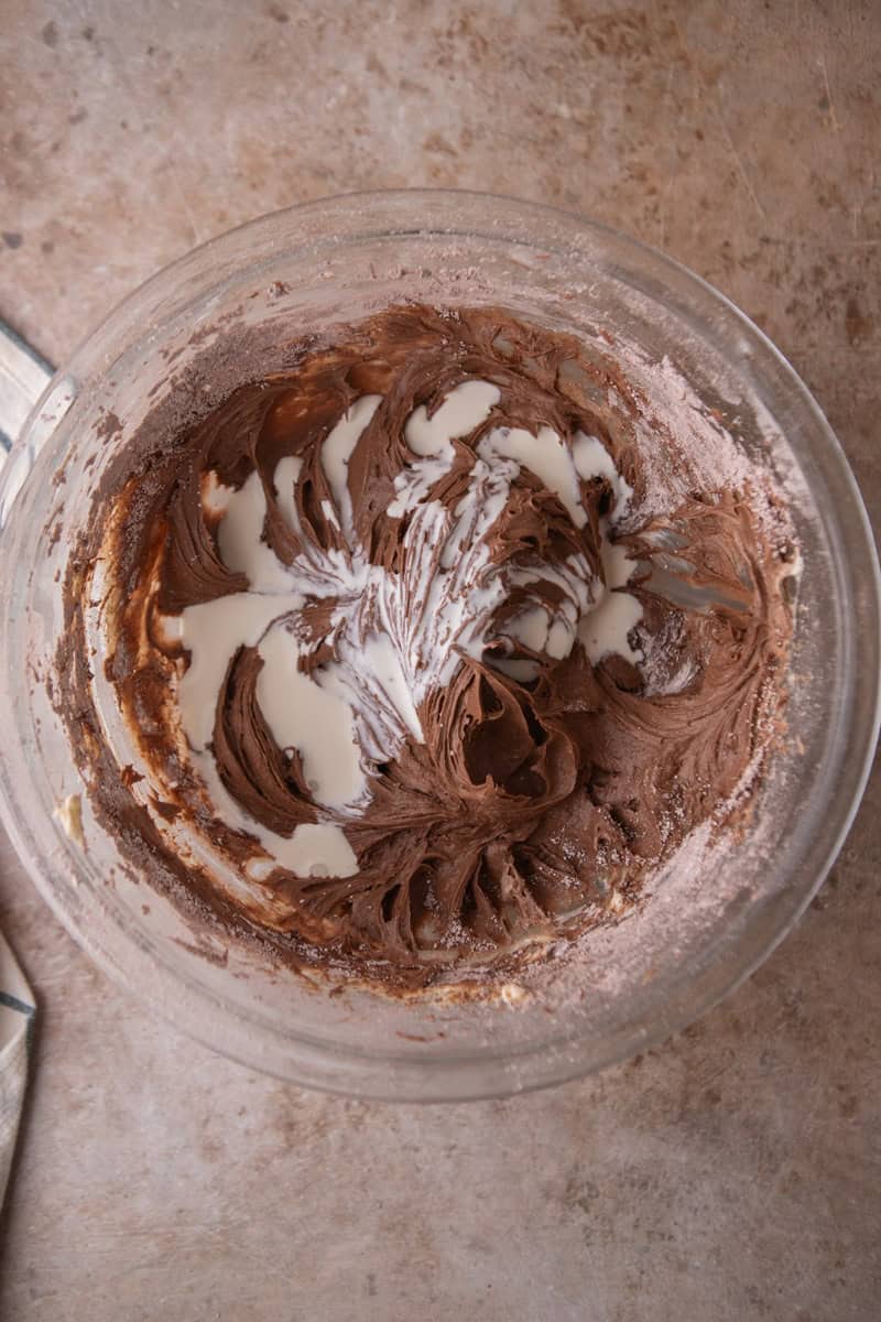 Heavy cream being added to the frosting while mixing in a glass bowl