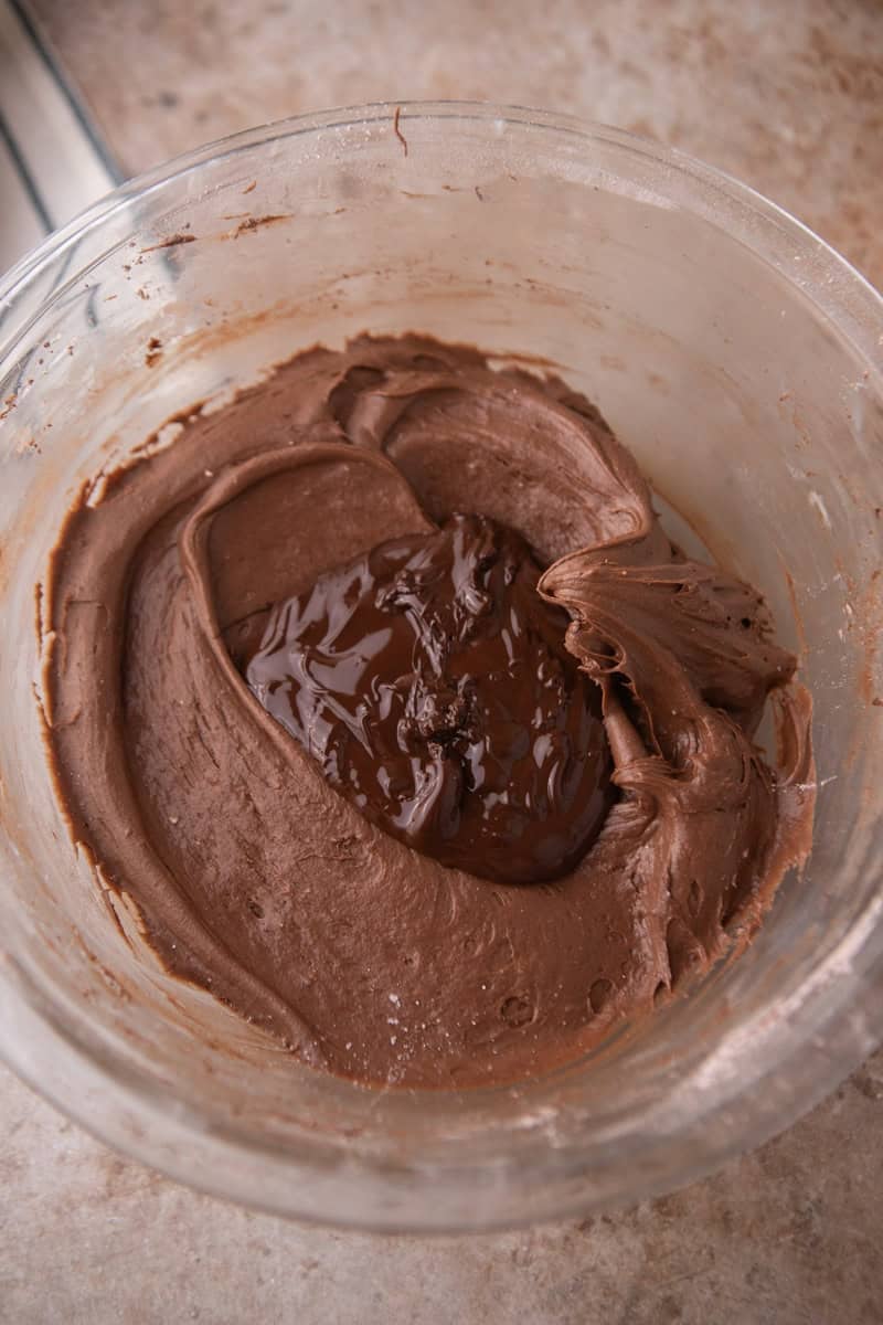 Melted dark chocolate added to the frosting in a glass bowl
