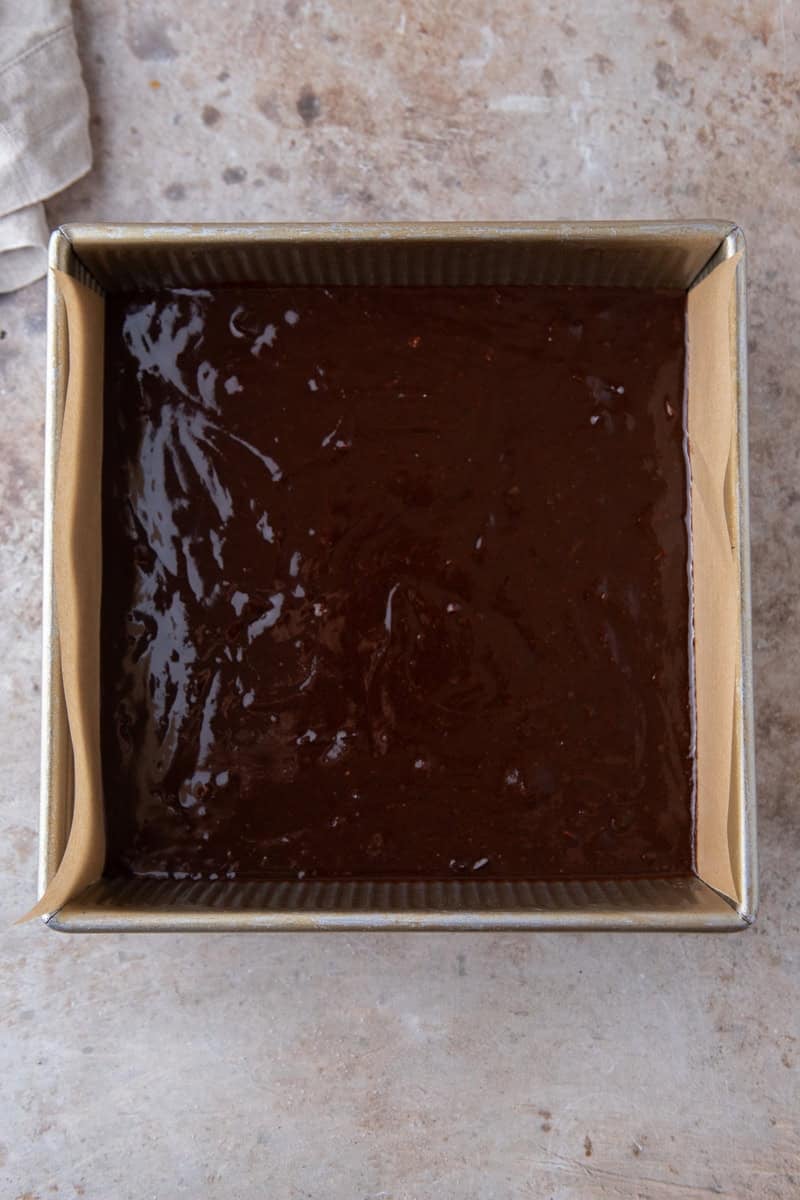 Espresso brownie batter poured into a parchment lined 8x8 metal baking pan