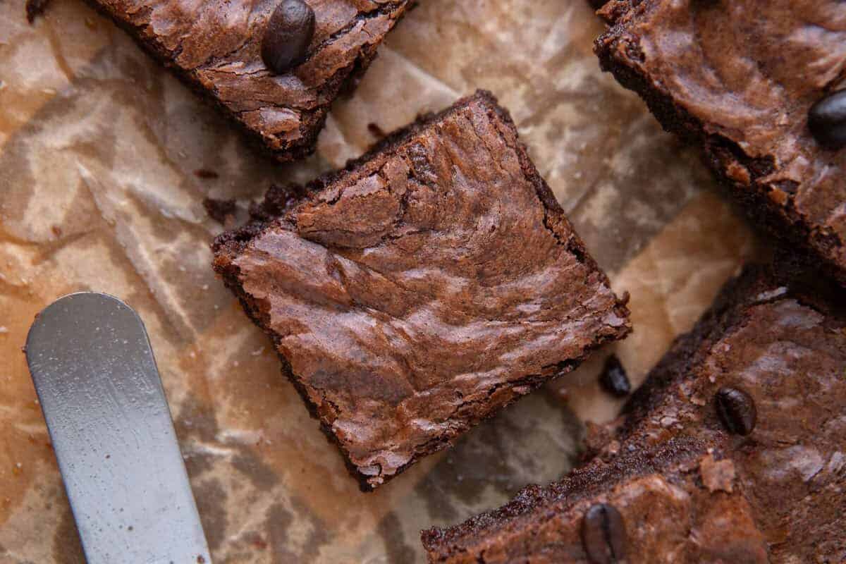 Fudgy espresso brownie square on crinkled parchment paper with an offset spatula