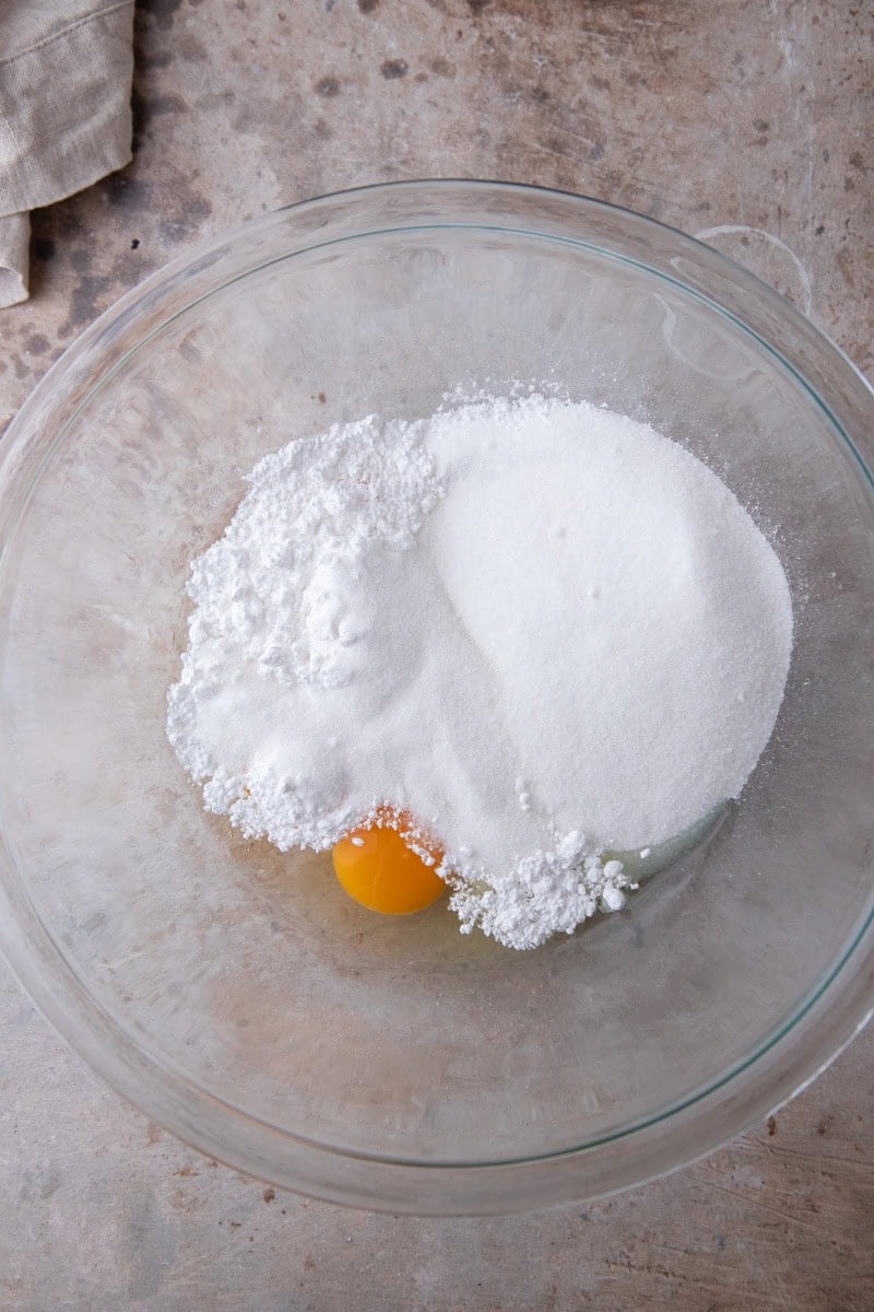 Eggs, granulated sugar, and powdered sugar in a glass mixing bowl before whipping