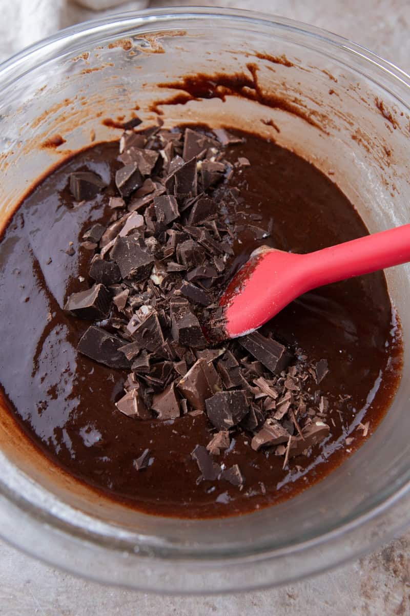 Folding chopped dark chocolate chunks into brownie batter with a red silicone spatula