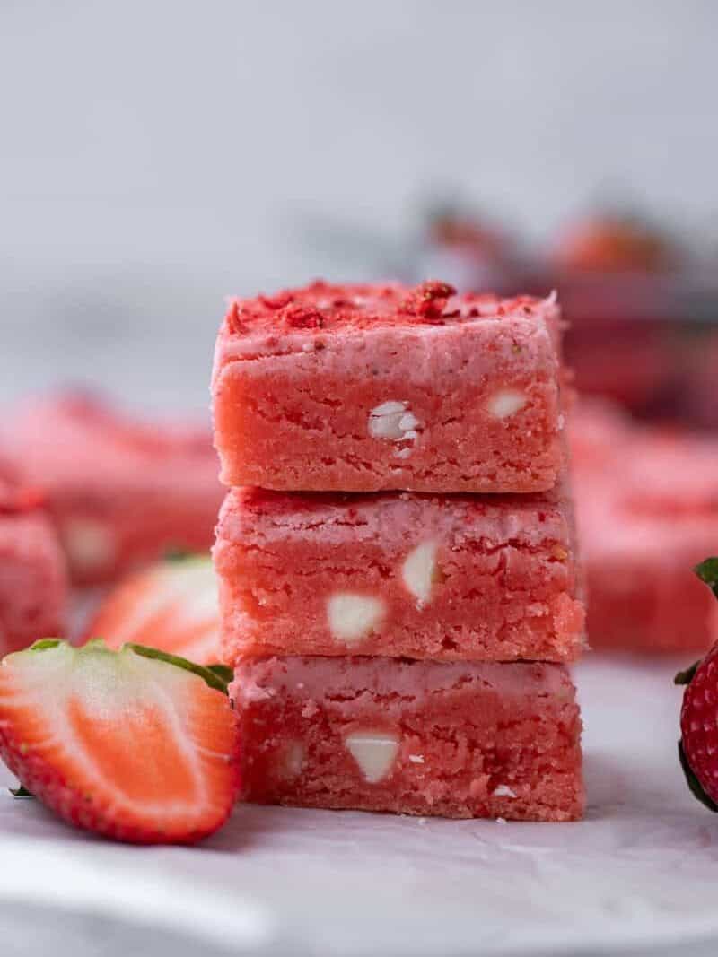 Pink strawberry cake mix brownies sliced into squares with one piece tilted to show the fudgy bright pink interior with melted white chocolate chips