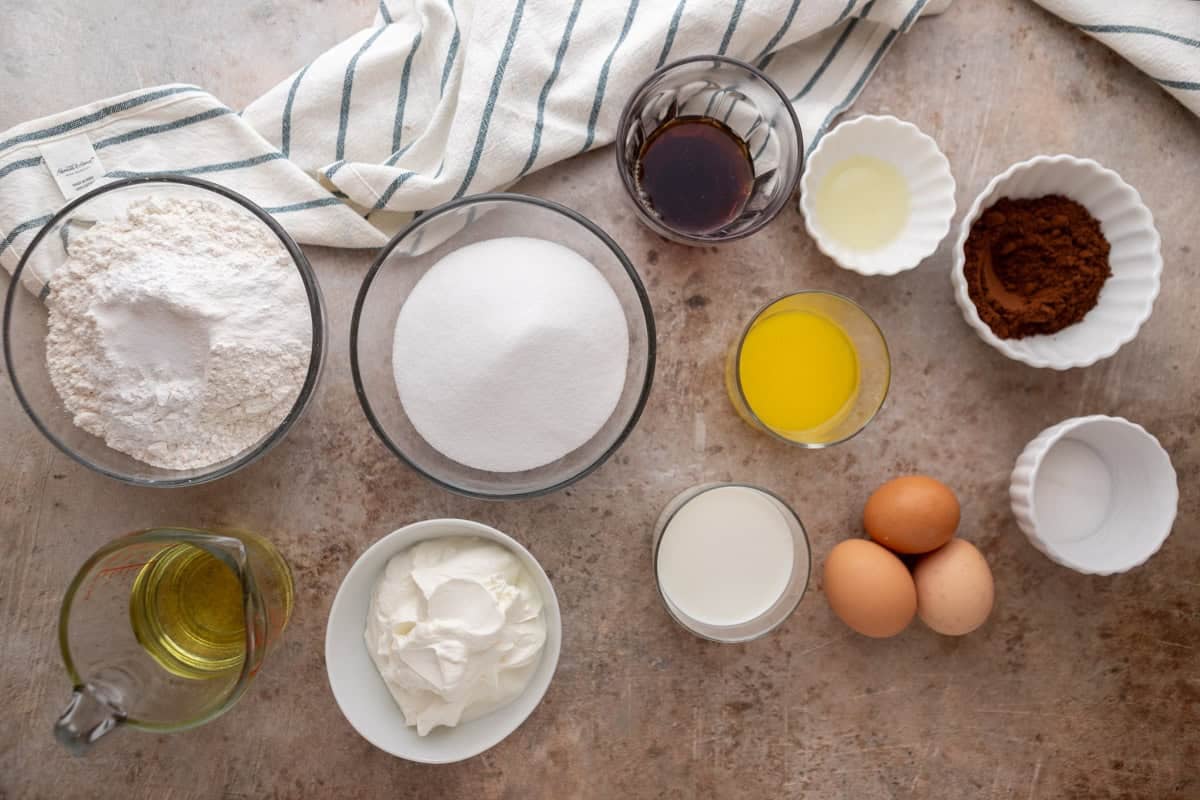 Ingredients including flour, sugar, eggs, sour cream, oil, melted butter, milk, vanilla, and cocoa powder