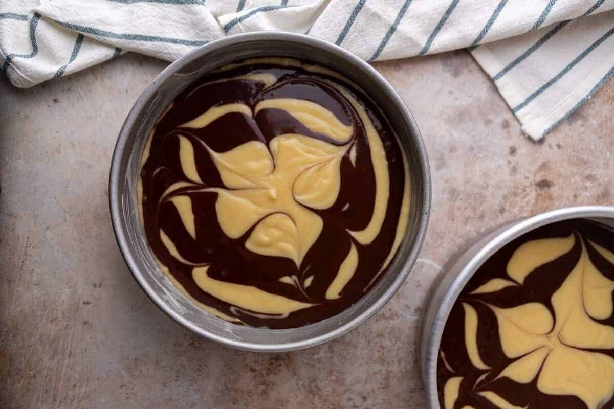 Vanilla and chocolate cake batter swirled together in two round cake pans before baking