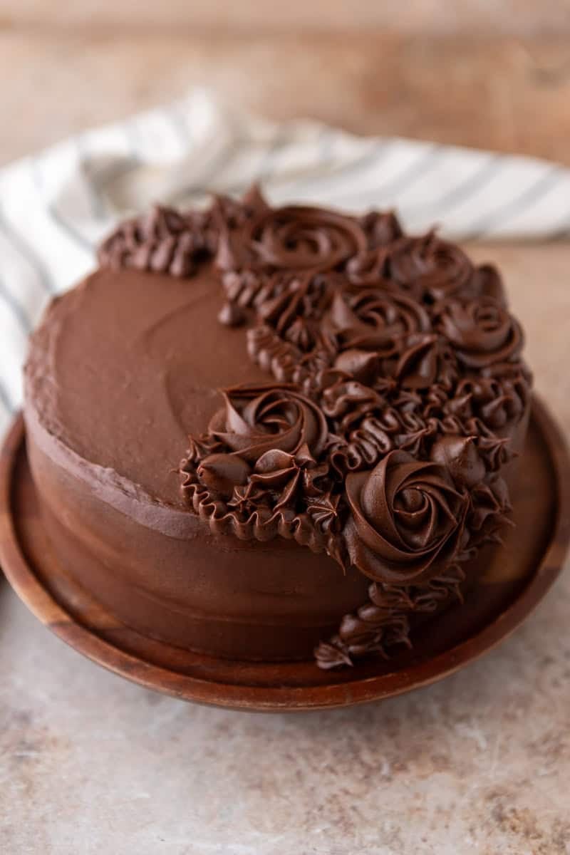 Finished layered marble cake frosted with chocolate cream cheese frosting and decorated with piped rosettes on a wooden plate