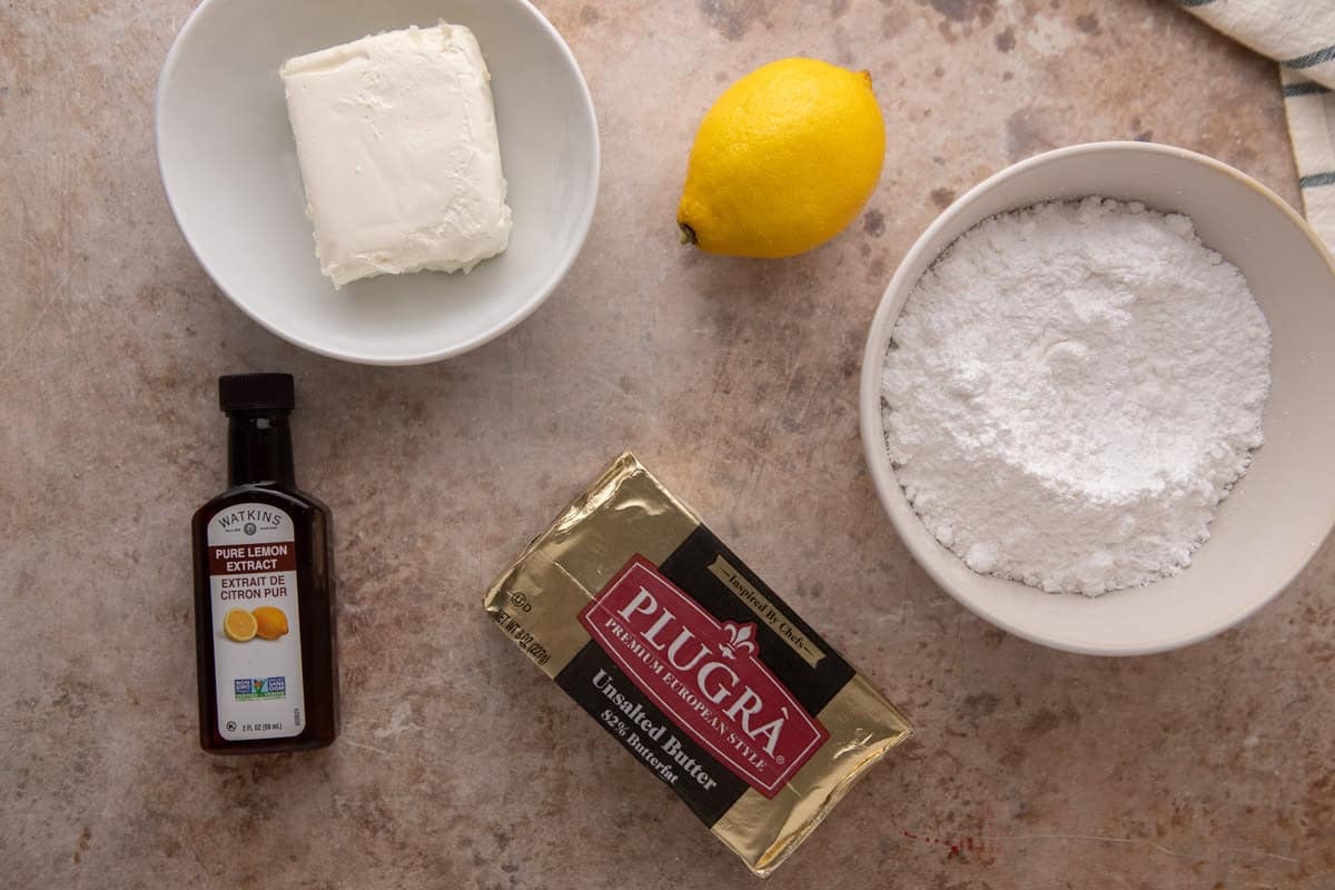 Cream cheese lemon frosting ingredients flatlay with Plugrà butter, cream cheese, powdered sugar, lemon, and lemon extract.