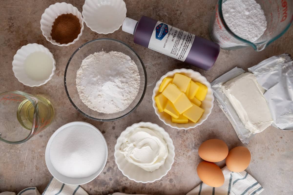 Ingredients arranged in bowls including flour, butter, sour cream, eggs, sugar, cocoa powder, and cream cheese.