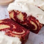 Thick slices of marble loaf cake with red velvet and vanilla swirls topped with cream cheese frosting.