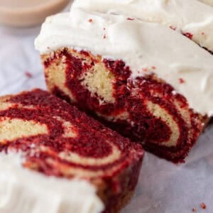 Thick slices of marble loaf cake with red velvet and vanilla swirls topped with cream cheese frosting.