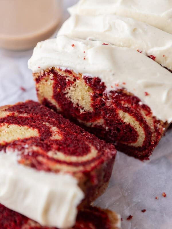 Thick slices of marble loaf cake with red velvet and vanilla swirls topped with cream cheese frosting.