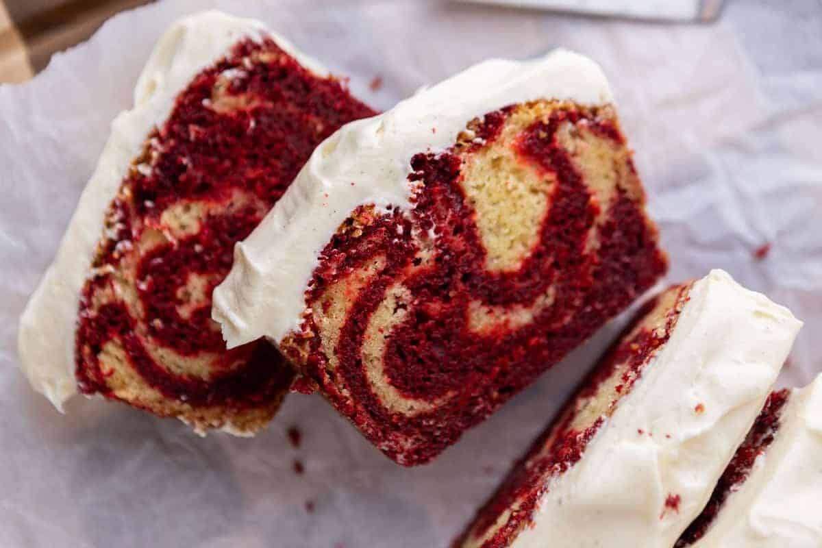 Sliced red velvet marble loaf cake with cream cheese frosting showing swirls of red and vanilla inside.