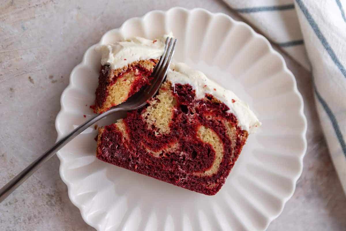 Thick slice of NY style red velvet loaf cake on a plate with a piece broken into with a fork