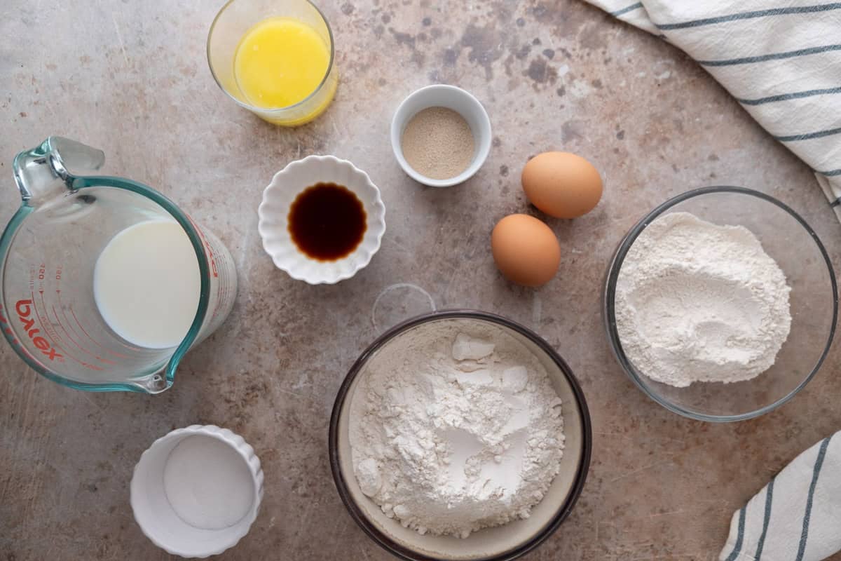 Ingredients for mini cinnamon roll dough including flour, bread flour, milk, melted butter, eggs, yeast, vanilla bean paste, and sugar