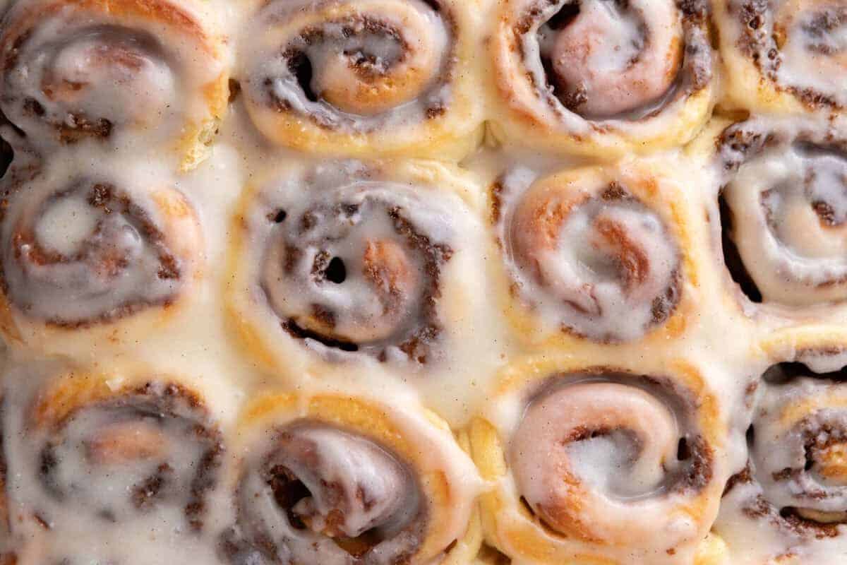 Mini cinnamon rolls with cream cheese glaze in a baking pan, close up showing visible cinnamon swirls