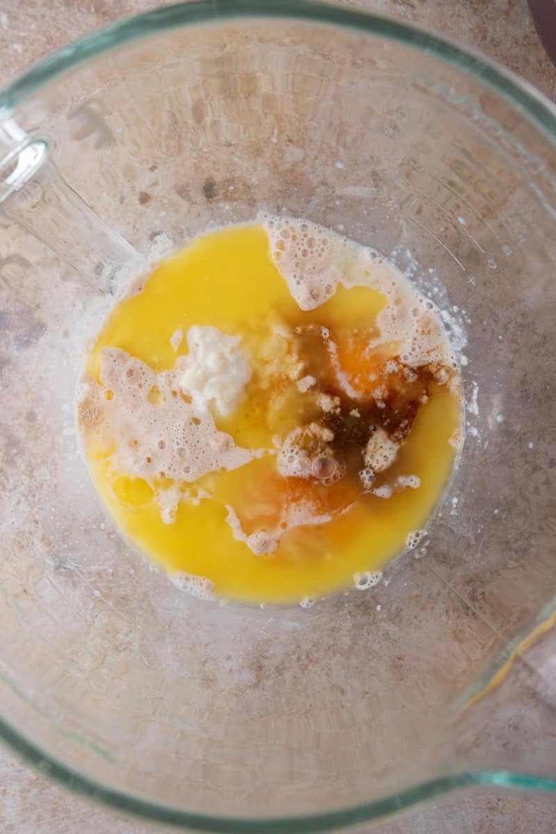 Wet ingredients for cinnamon roll dough in a glass mixing bowl including melted butter, eggs, tangzhong, and activated yeast mixture