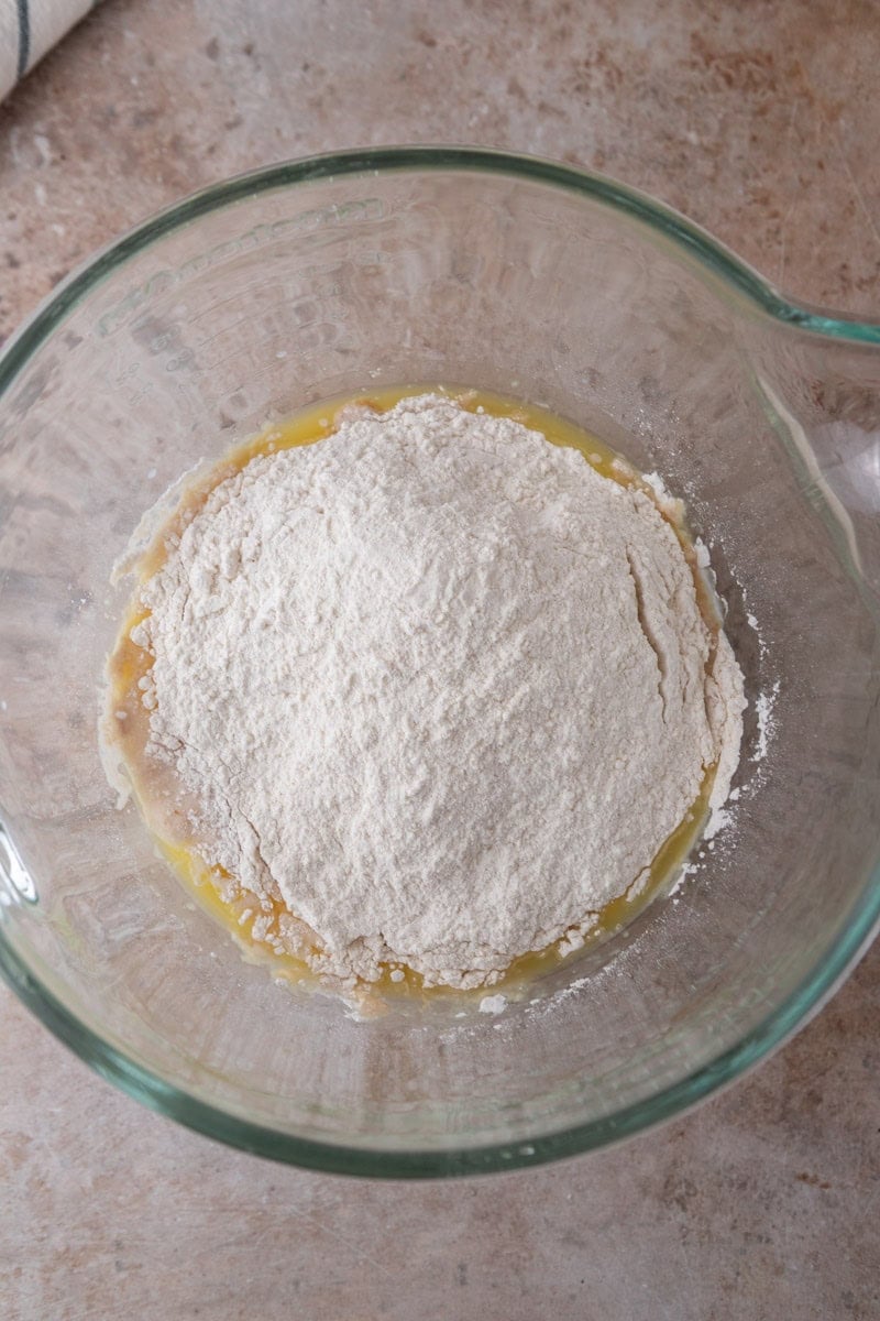 All purpose flour and bread flour added on top of wet ingredients in a glass mixing bowl
