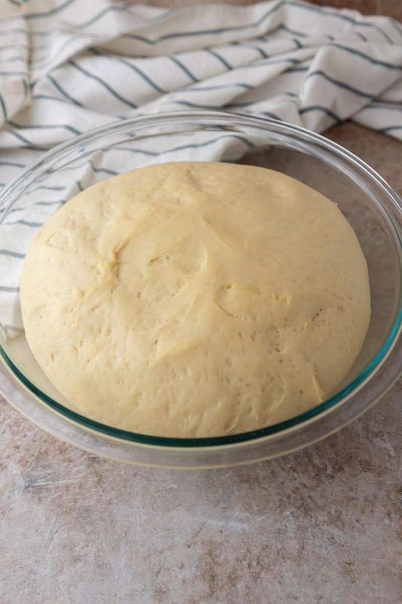 Risen cinnamon roll dough doubled in size in a glass bowl