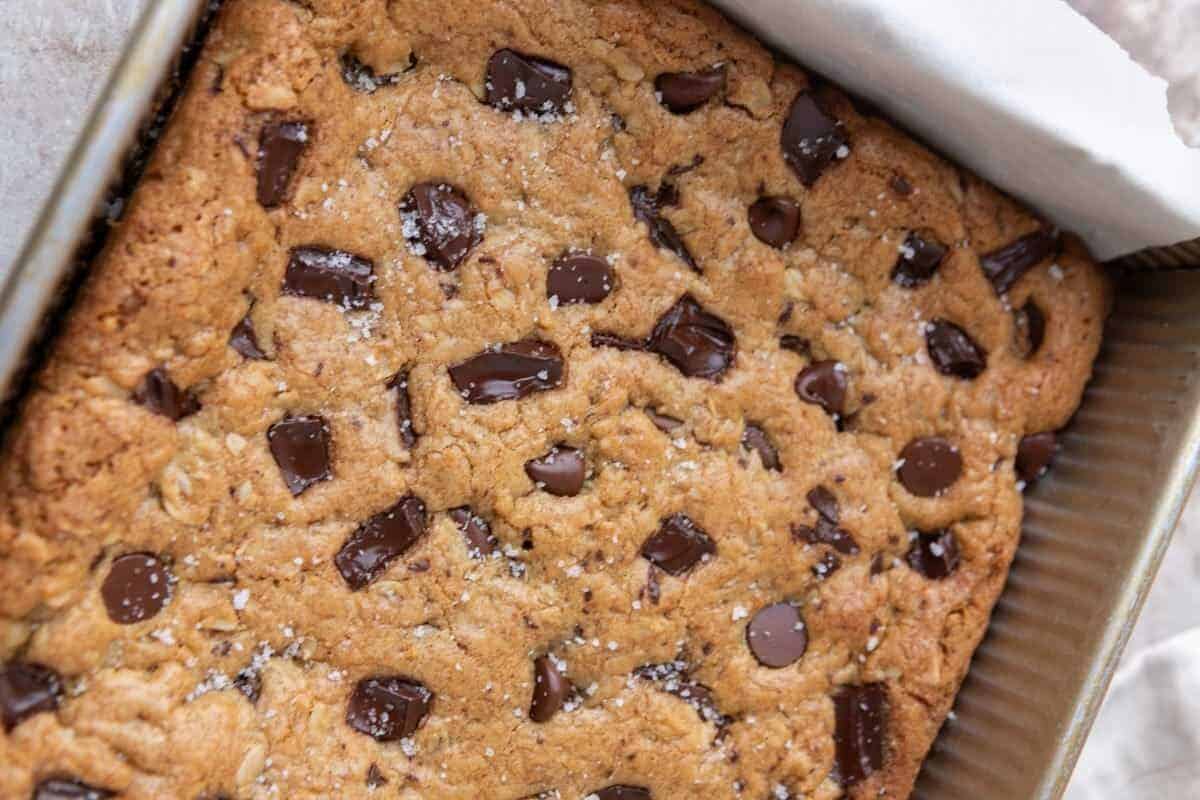 Freshly baked oatmeal cookie bar slab in a parchment-lined 8x8 baking pan topped with flaky salt