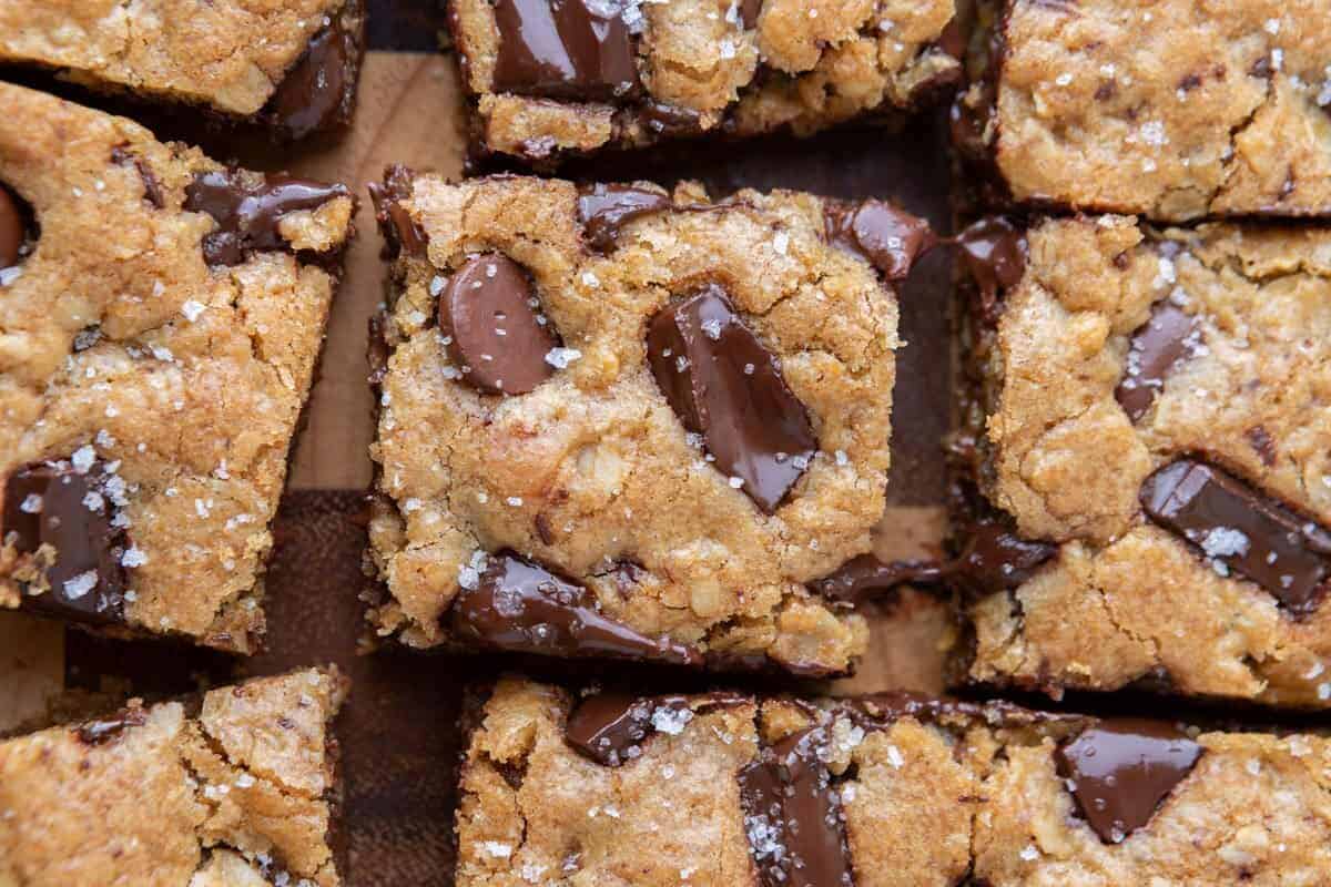 Overhead view of sliced oatmeal chocolate chip cookie bars with melted chocolate chunks and flaky salt on a wooden board