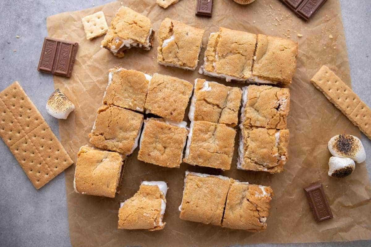 Sliced s'mores cookie bars on a counter showing the layered cross-section of graham cracker cookie dough, chocolate, and marshmallow