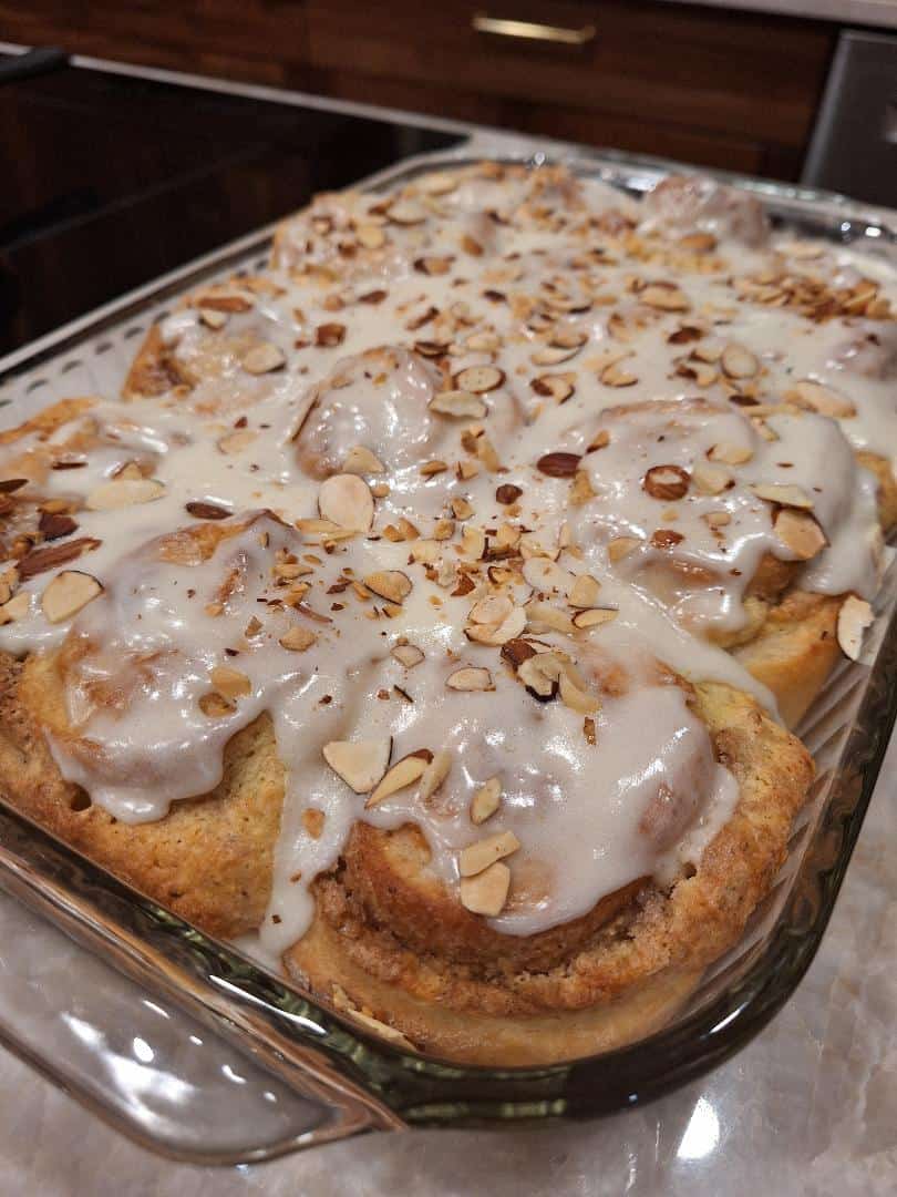 Pan of glazed almond cinnamon rolls topped with sliced almonds, a Loaf BakeClub featured recipe