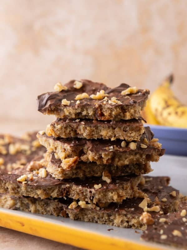 Stack of banana bread Christmas crack pieces on a plate with a banana in the background.