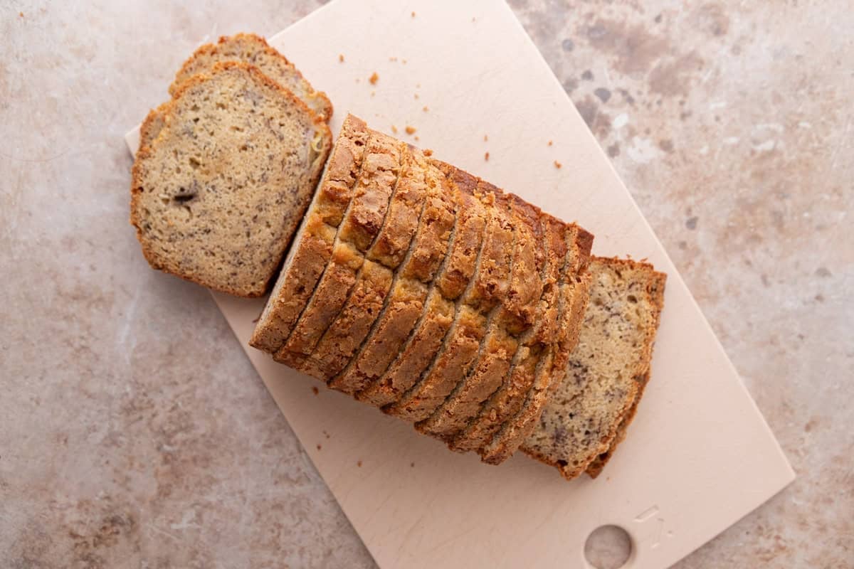 Loaf of banana bread thinly sliced on a wooden cutting board ready to be turned into Christmas crack.