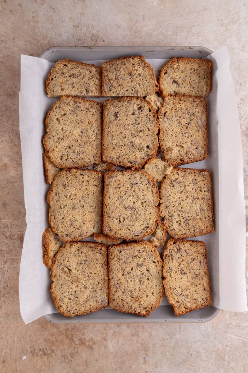 Thin slices of banana bread arranged on a parchment lined tray for Christmas crack.