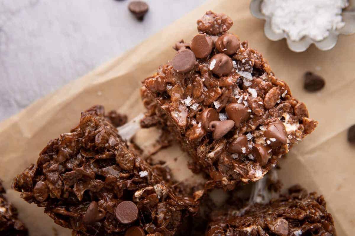 Sliced chocolate rice krispie treats stacked on parchment paper with chocolate chips and flaky sea salt on top
