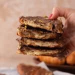 Hand holding a tall stack of croissant Christmas crack pieces with visible flaky layers and gold leaf