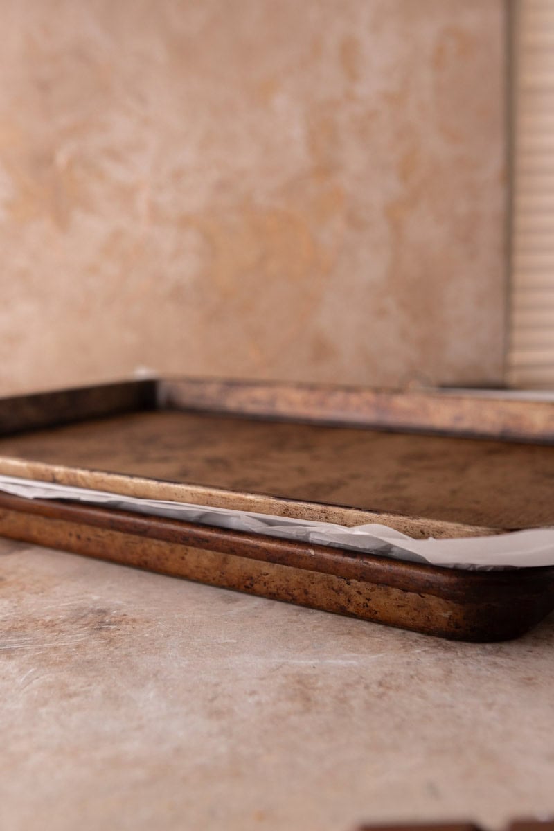 Two baking sheets stacked with parchment between to press croissants flat for croissant Christmas crack