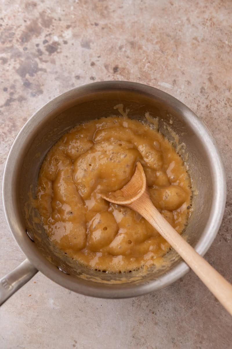 Brown sugar toffee bubbling in a saucepan with a wooden spoon, ready to pour over croissants
