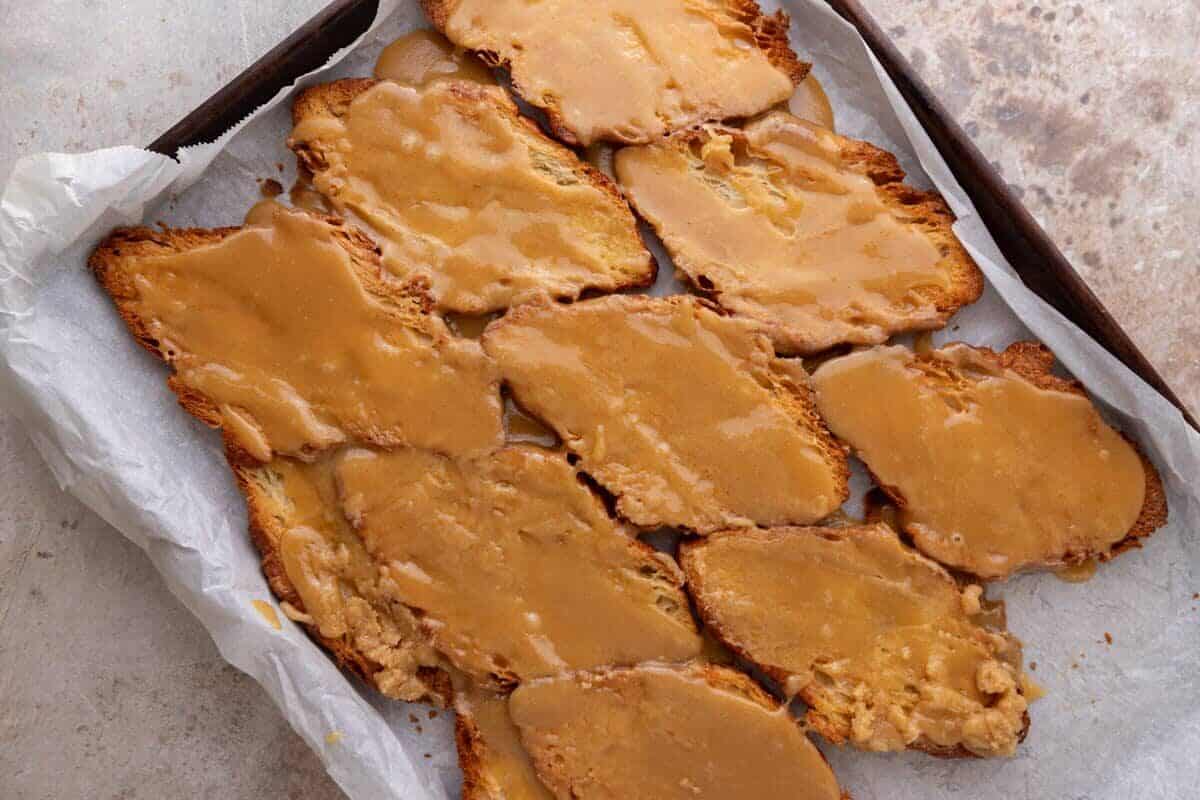 Brown sugar toffee spread over toasted pressed croissants on a parchment-lined sheet pan