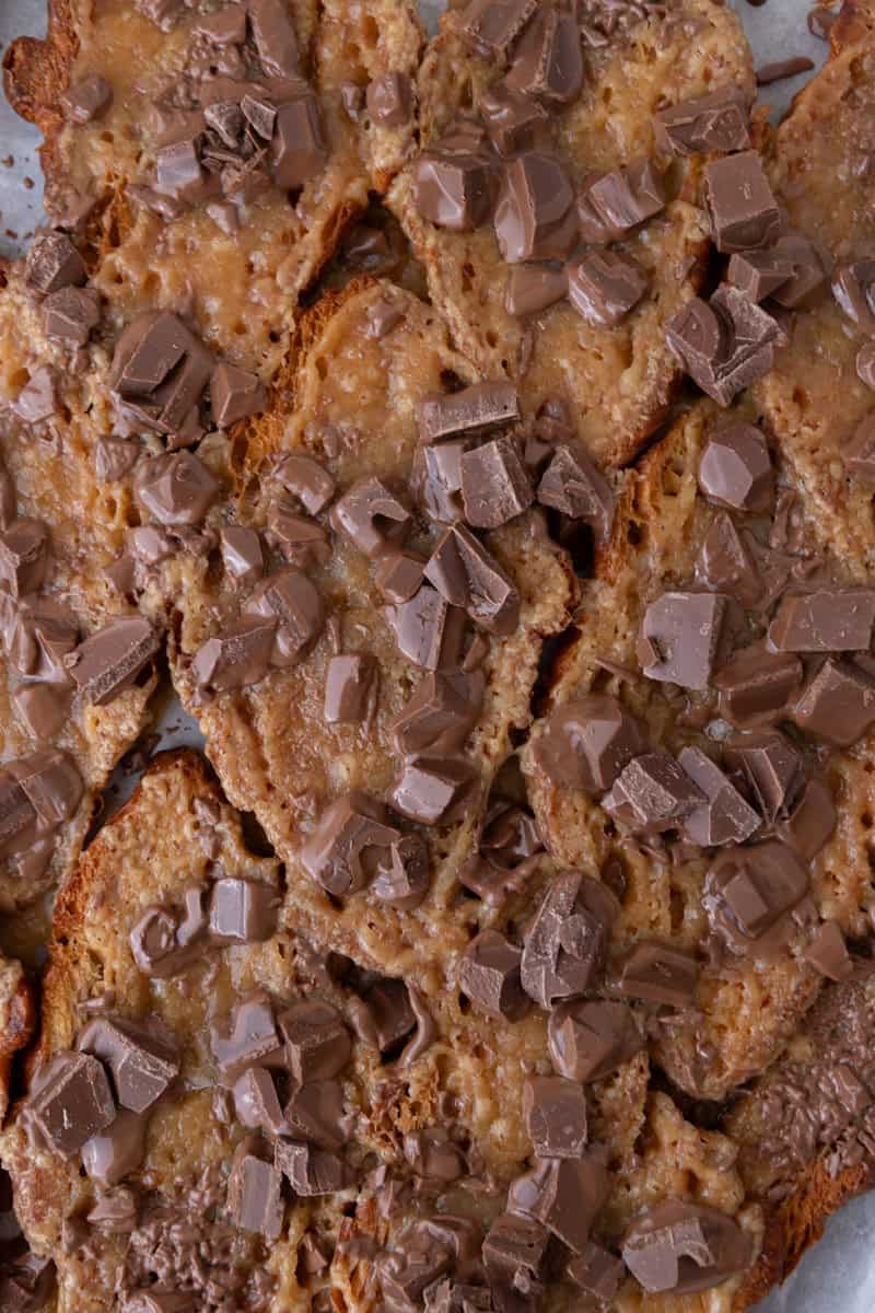 Chopped chocolate scattered over brown sugar toffee on pressed croissants for Christmas crack