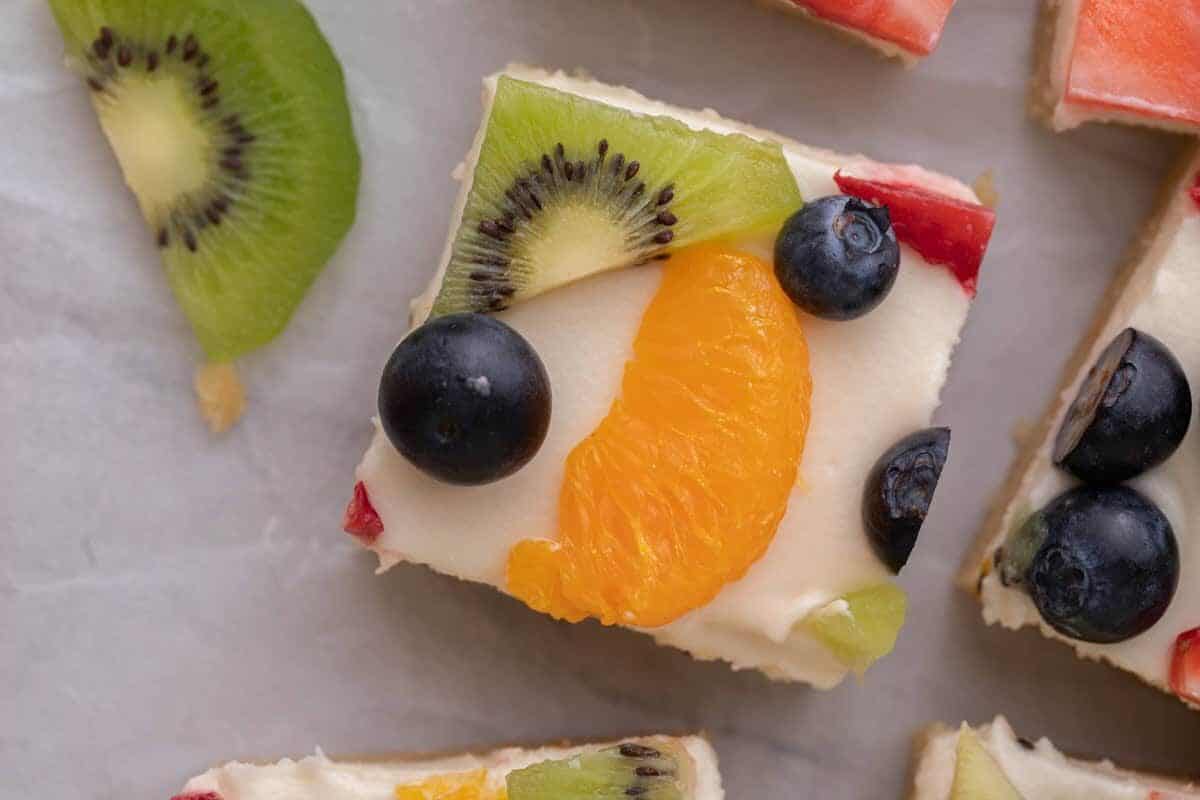 Two fruit pizza bars stacked to show the soft sugar cookie crust, cream cheese frosting layer, and fresh fruit topping