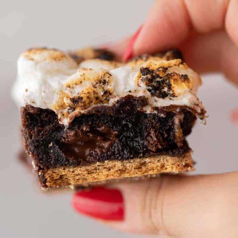 Hand holding a fudgy s'mores brownie with toasted marshmallow topping