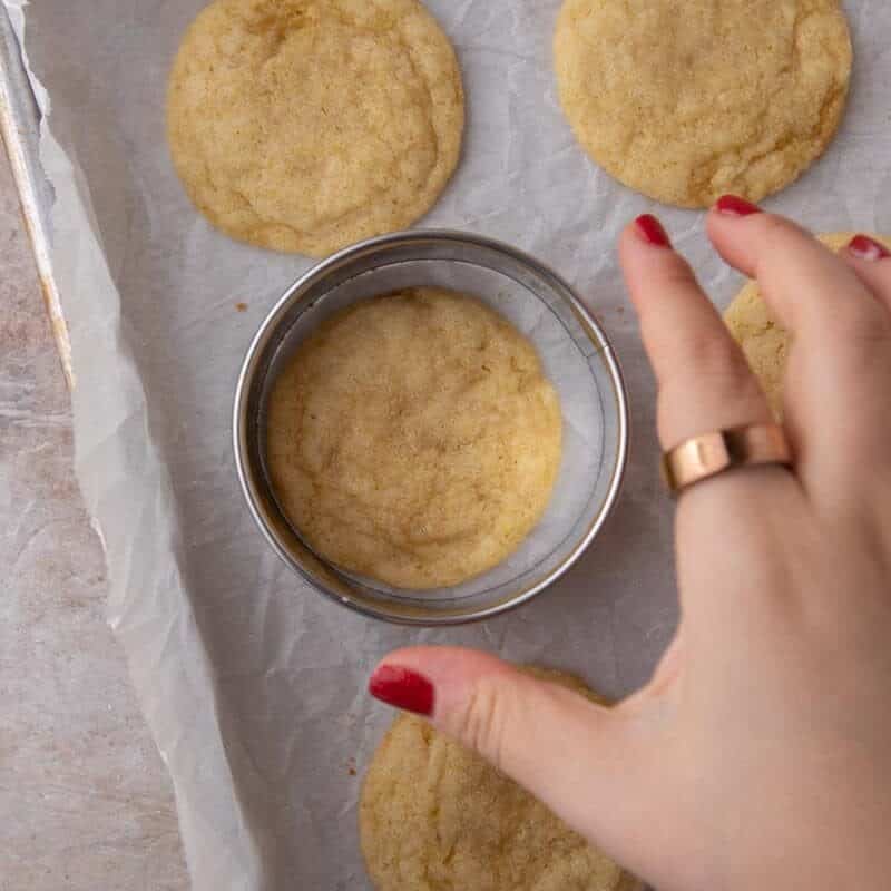 Round cookie cutter being used to swish a freshly baked lemon cookie back into a perfect circle.