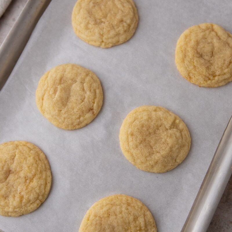 Freshly baked lemon sugar cookies cooling on a parchment-lined baking sheet.