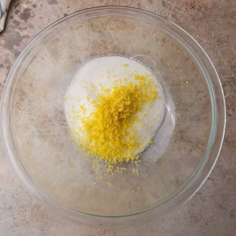 Glass bowl with granulated sugar and fresh lemon zest before being rubbed together to release oils.