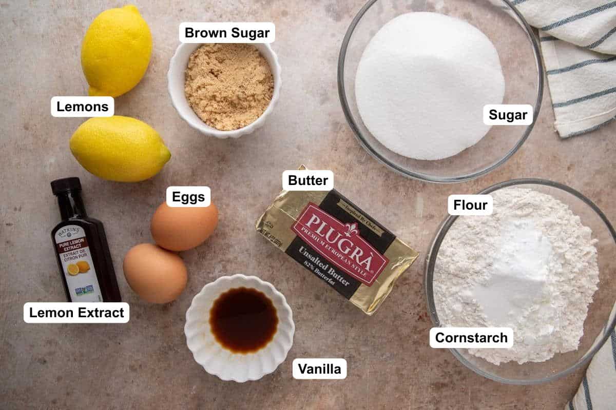 Overhead flat lay of lemon sandwich cookie ingredients including Plugrà butter, lemons, eggs, sugar, flour, and lemon extract.