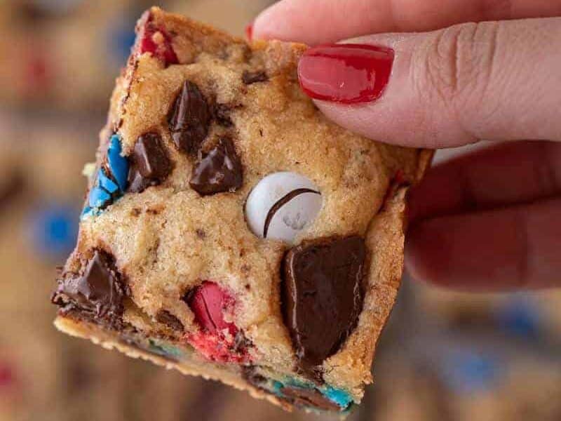 Hand holding a patriotic m&m's blondie square showing the fudgy chewy interior with red, white, and blue M&M's on top